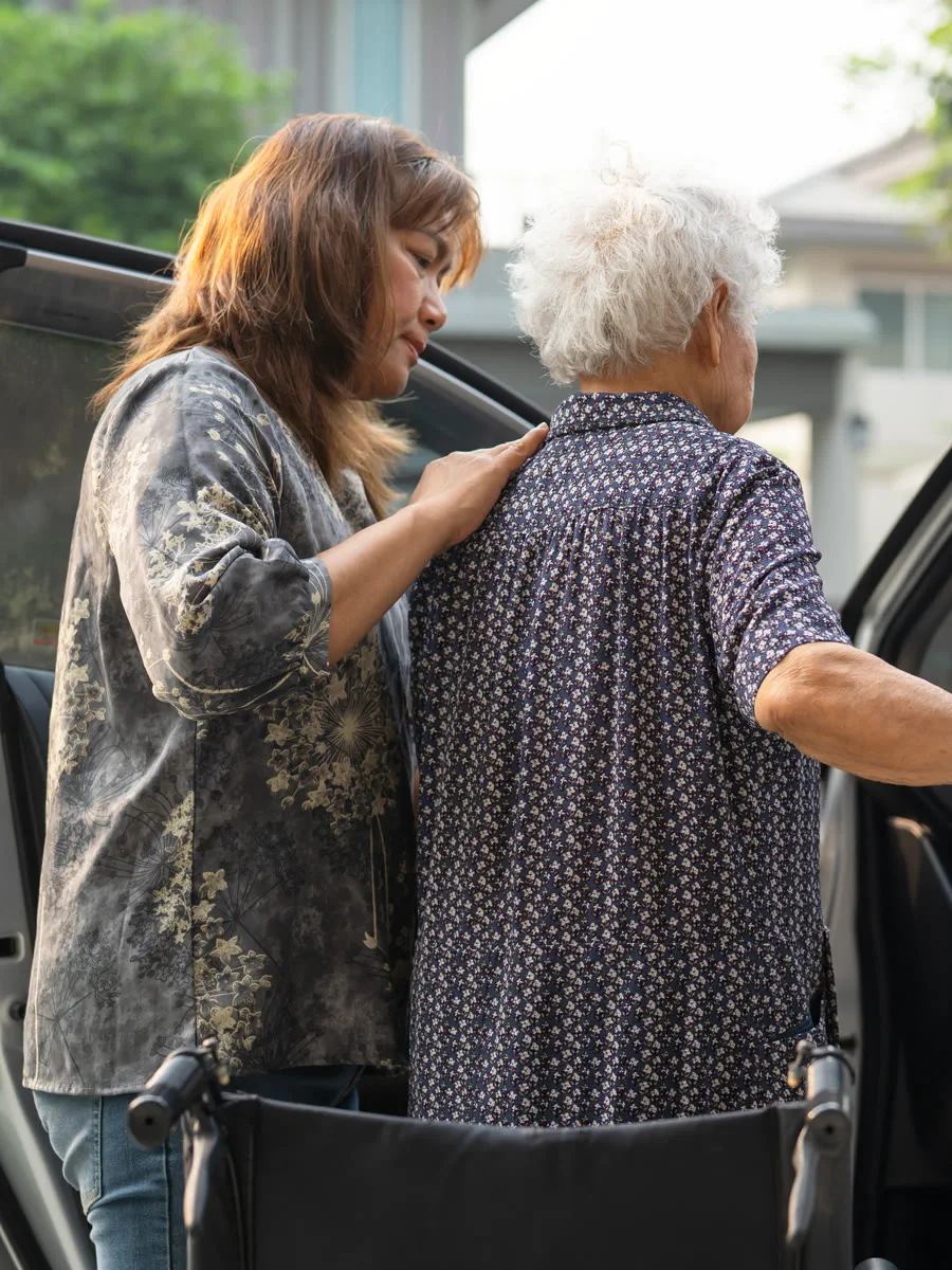 Cuidadora auxiliando uma senhora idosa a entrar no carro com segurança